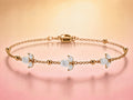 A delicate gold chain bracelet with three decorative floral motifs set with clear stones, displayed on a soft pink and gold gradient background.
