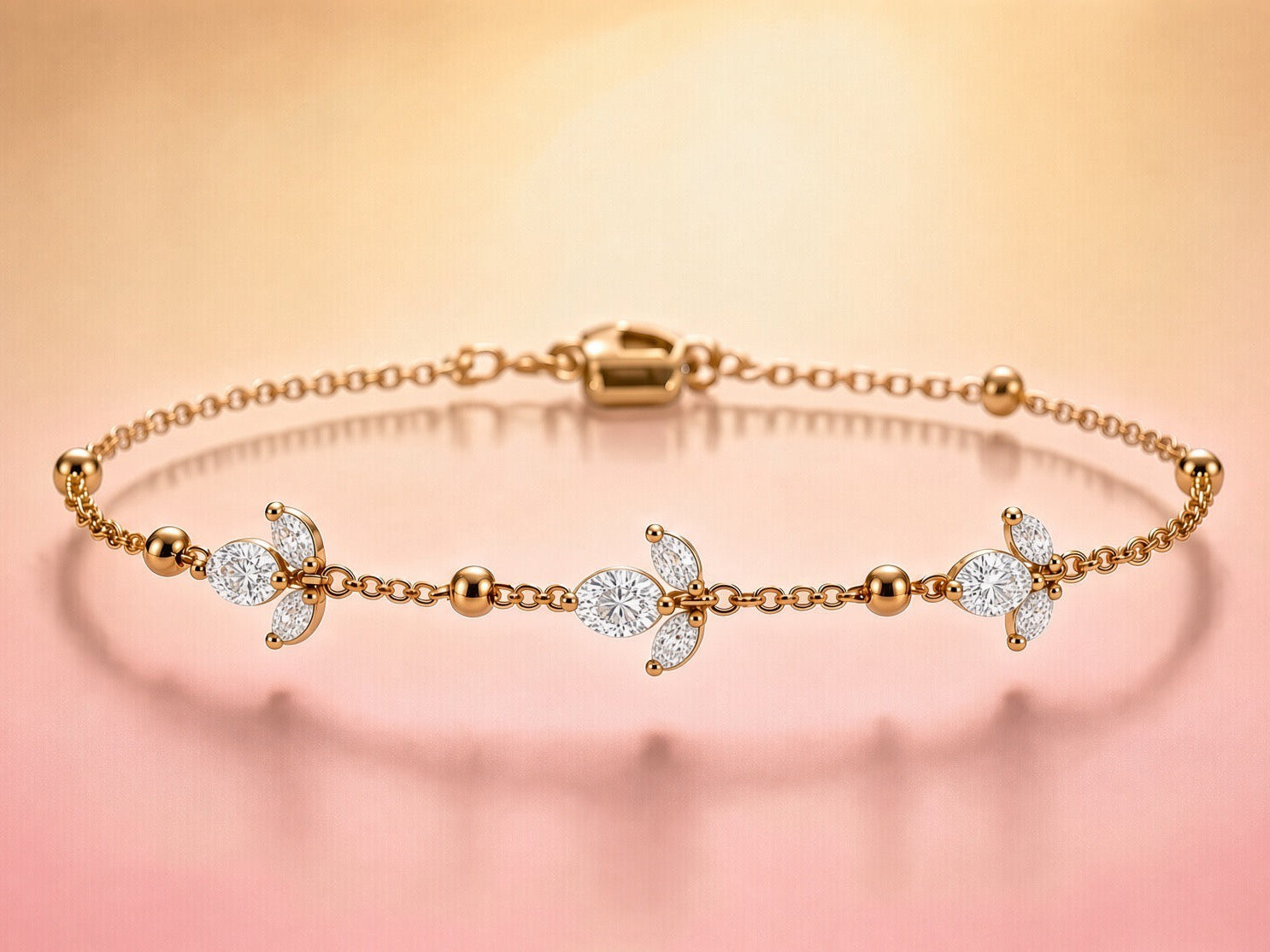 A delicate gold chain bracelet with three decorative floral motifs set with clear stones, displayed on a soft pink and gold gradient background.
